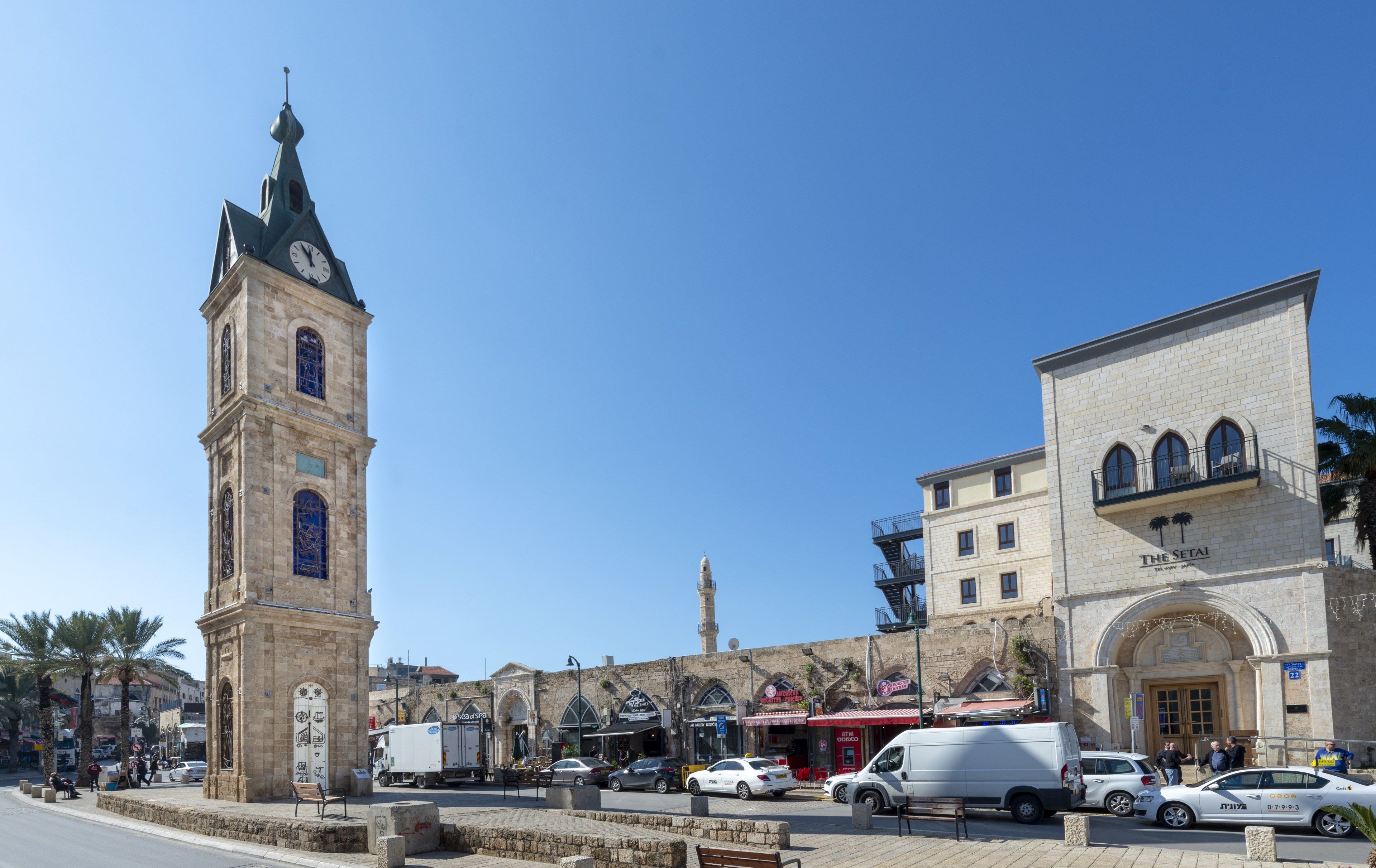 Une tour de l’horloge historique, un bâtiment portant une enseigne indiquant « The Setai », et une rue animée par des voitures et des piétons.