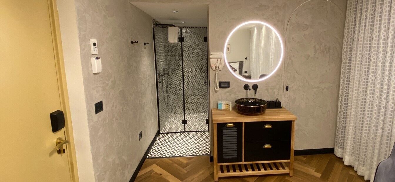 A bathroom with a wooden vanity, a round mirror, and a shower area with a patterned wall.
