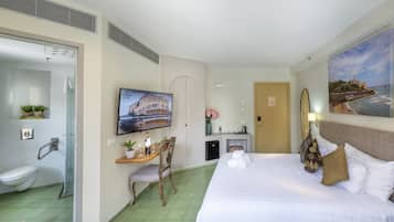 A hotel room with a bed, a desk with a chair, a television, a bathroom, and a painting on the wall.