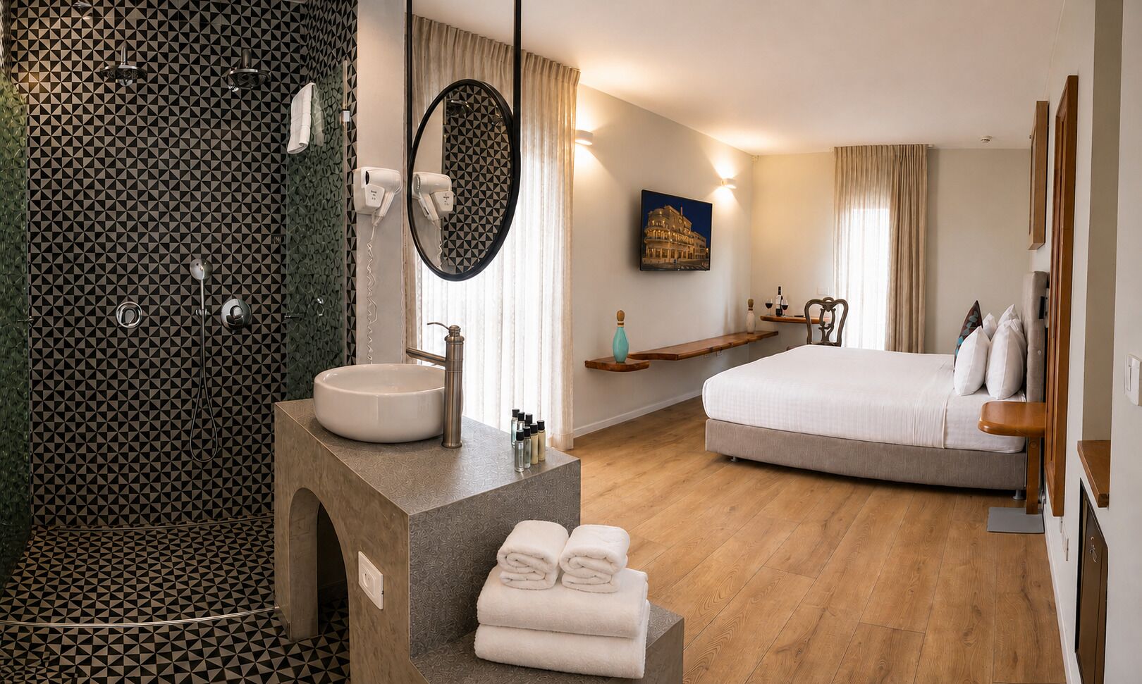 A modern hotel room with a shower, a sink, a bed, and a painting on the wall.
