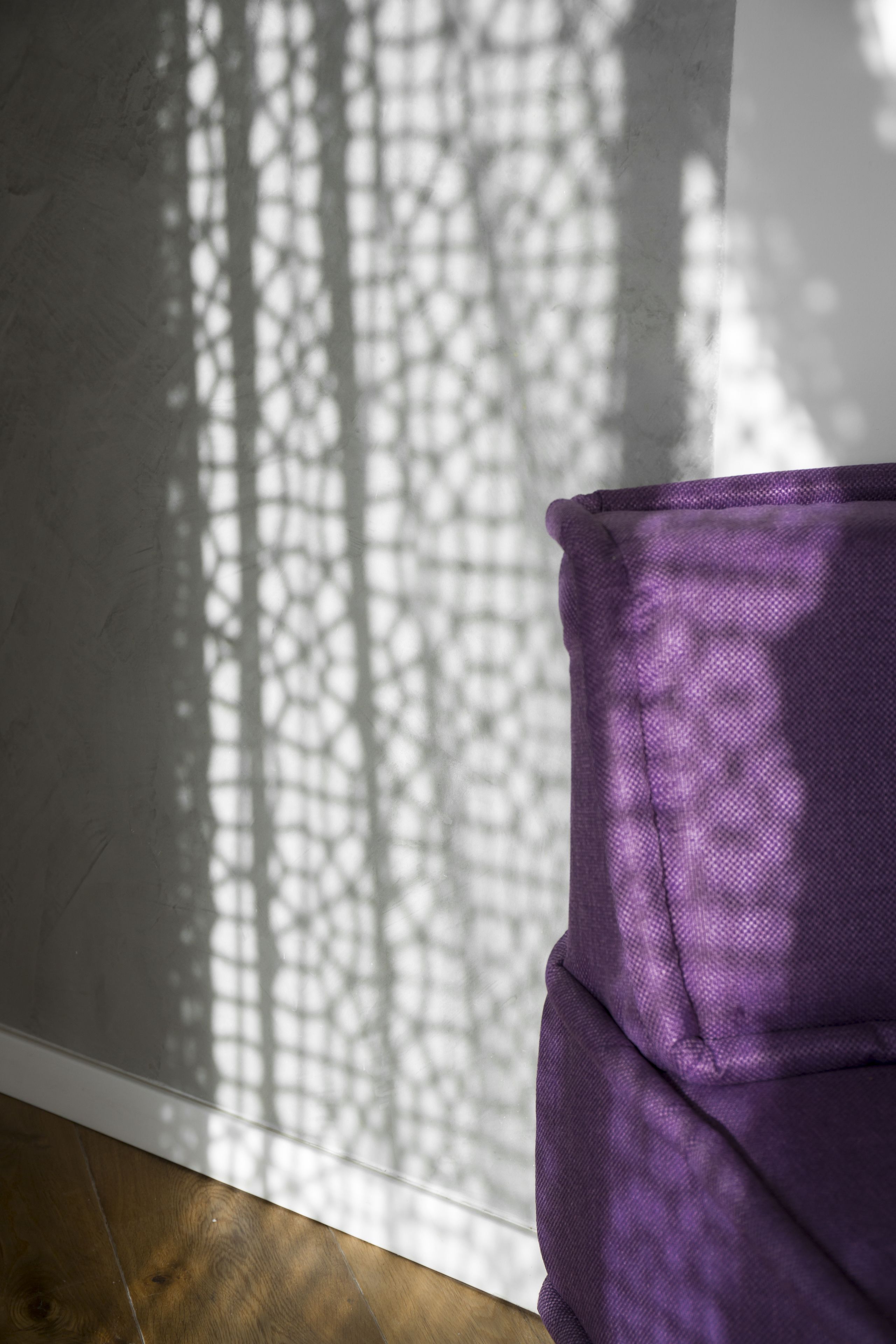 Una habitación con una ventana que proyecta un entramado de luces y sombras sobre un objeto de tela púrpura.