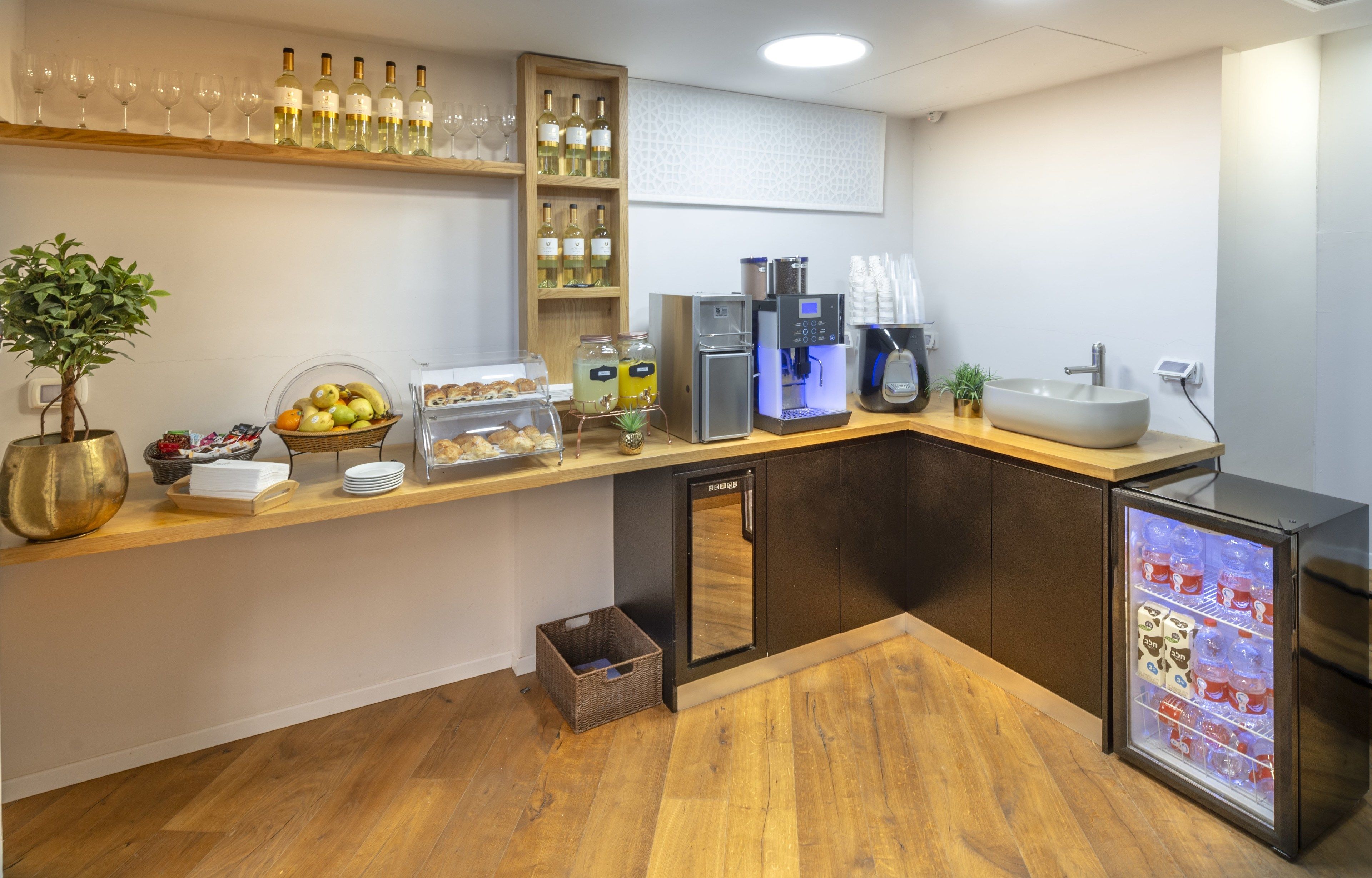 Cozinha moderna com bancada de madeira, garrafas de vinho, máquina de café, geladeira e cesta de frutas.