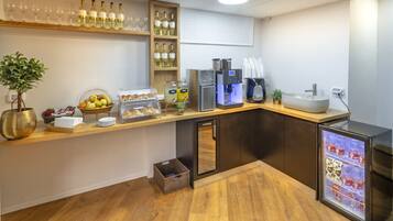 Un espace cuisine moderne avec un comptoir en bois, des bouteilles de vin, une machine à café, un réfrigérateur et un panier de fruits.