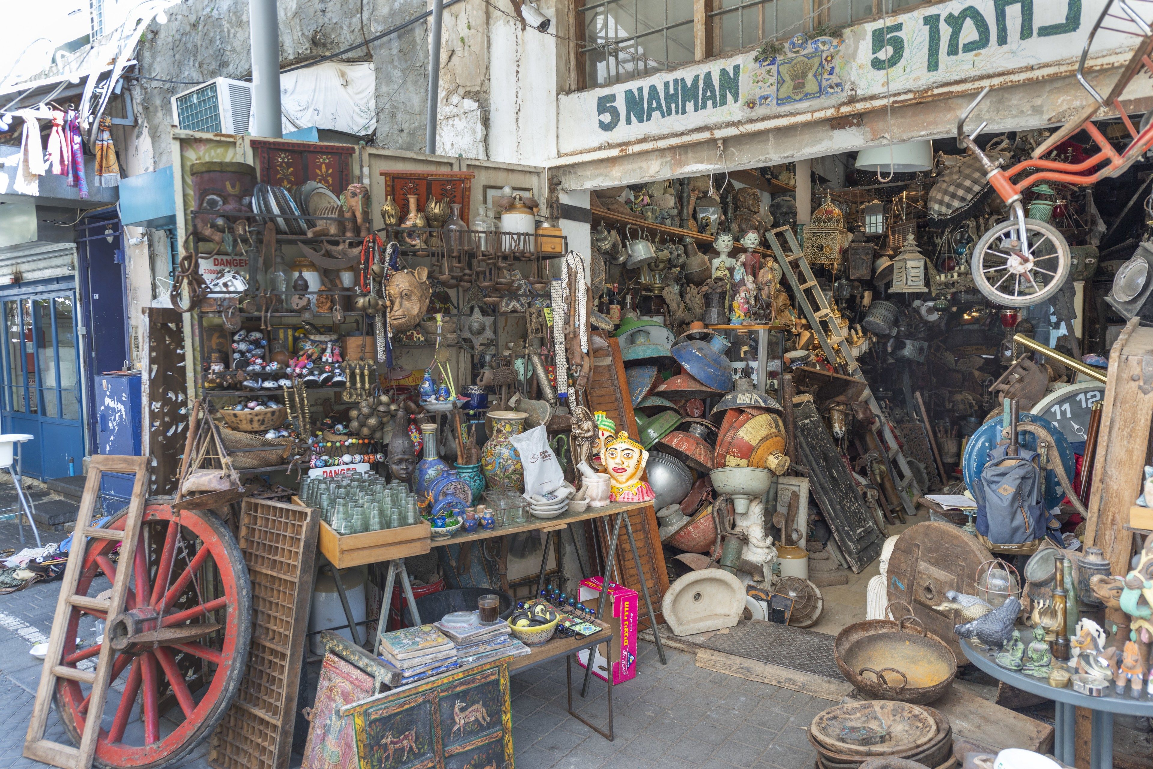A cluttered outdoor market with various items for sale, including pottery, toys, and household items.