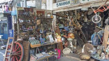 A cluttered outdoor market with various items for sale, including pottery, toys, and household items.