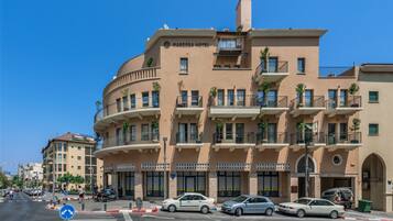 Un hotel de varios pisos con balcones, un cielo azul despejado y una calle con coches aparcados.