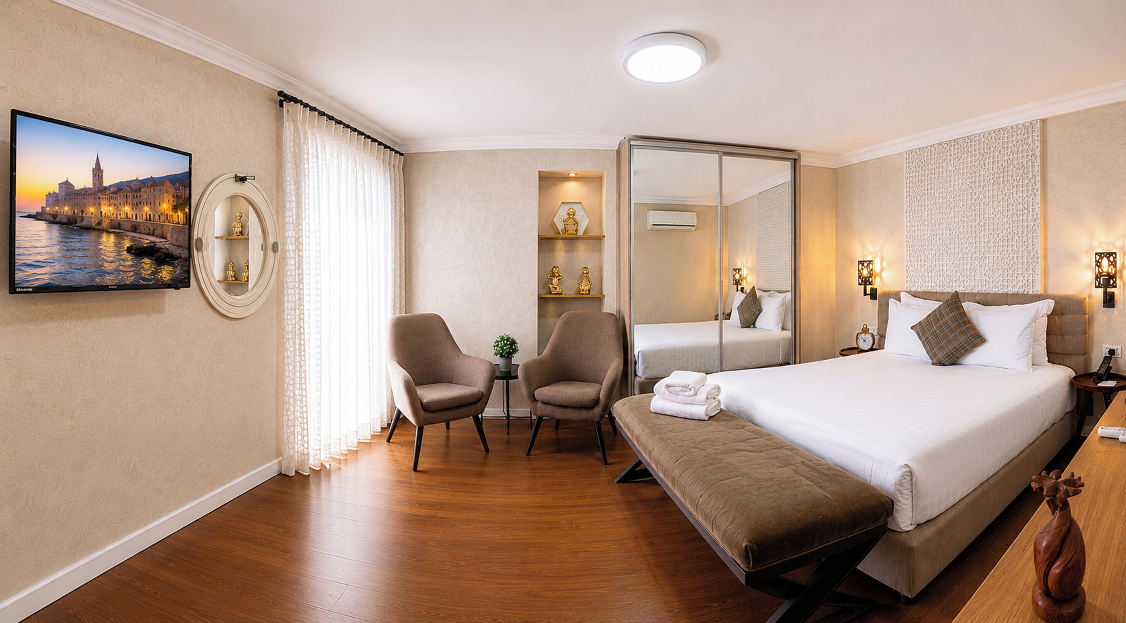 A hotel room with a bed, two armchairs, a small table, a mirror, and a painting of a cityscape.