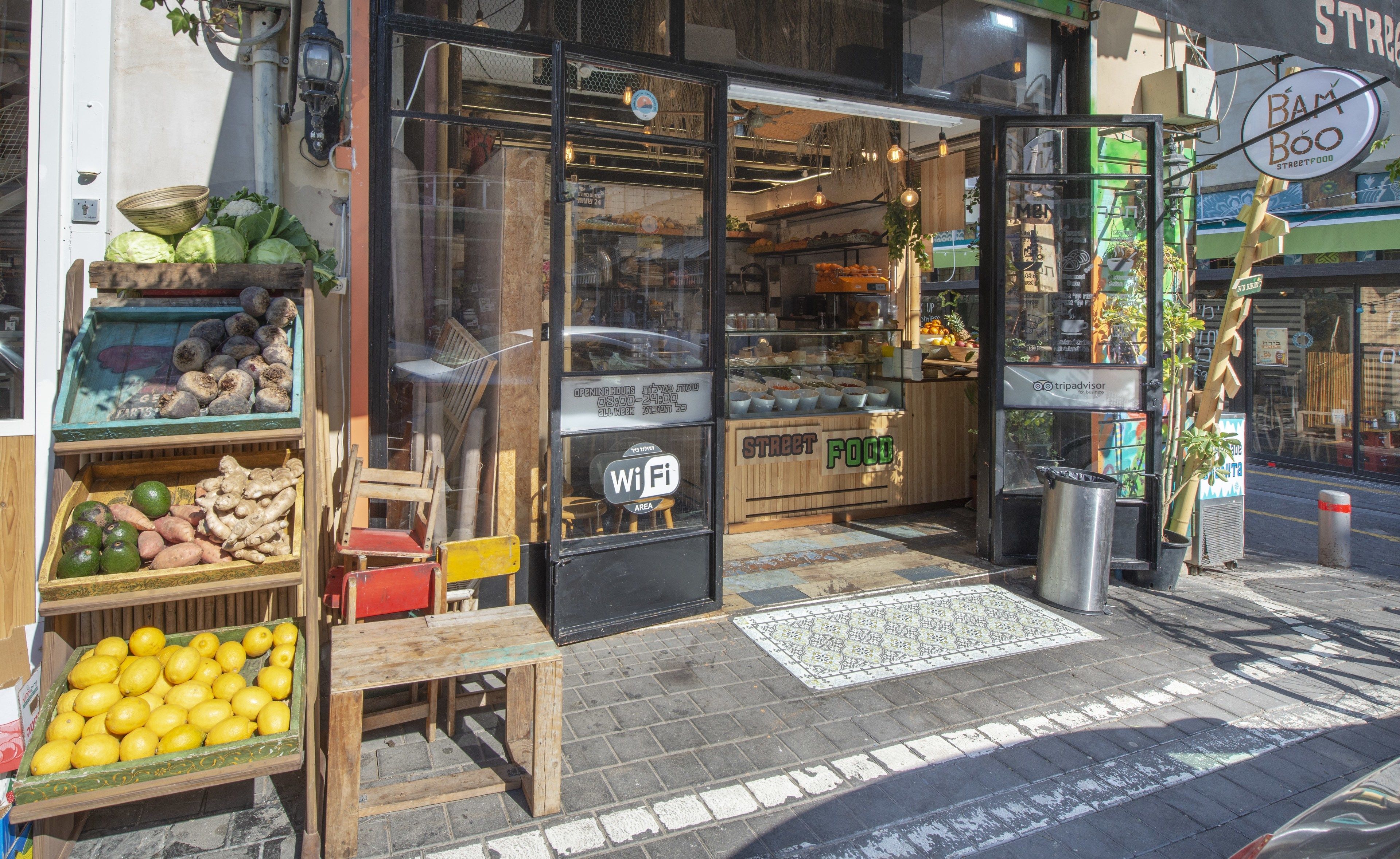 Un puesto de comida callejera con gran variedad de frutas y verduras frescas y una mesa de madera al exterior.