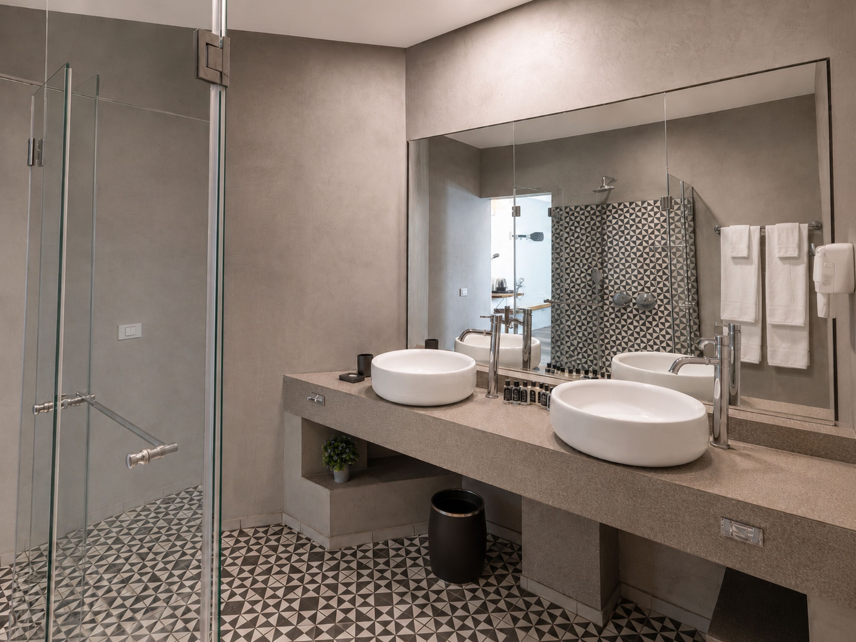 A modern bathroom with a glass shower enclosure, a large mirror, and two sinks.