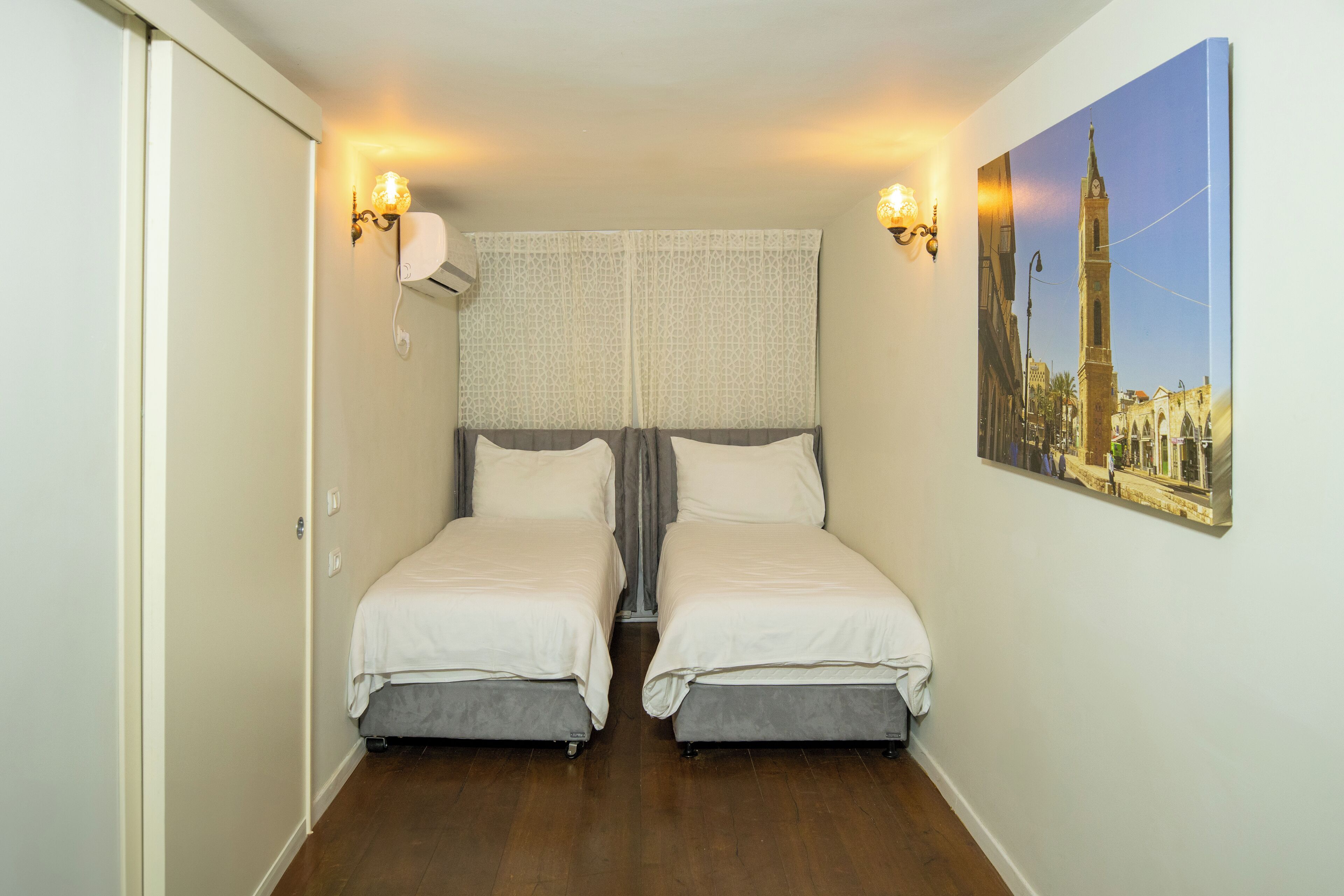 Una habitación con dos camas, una cortina estampada, un cuadro de una torre y luces fijadas en la pared.
