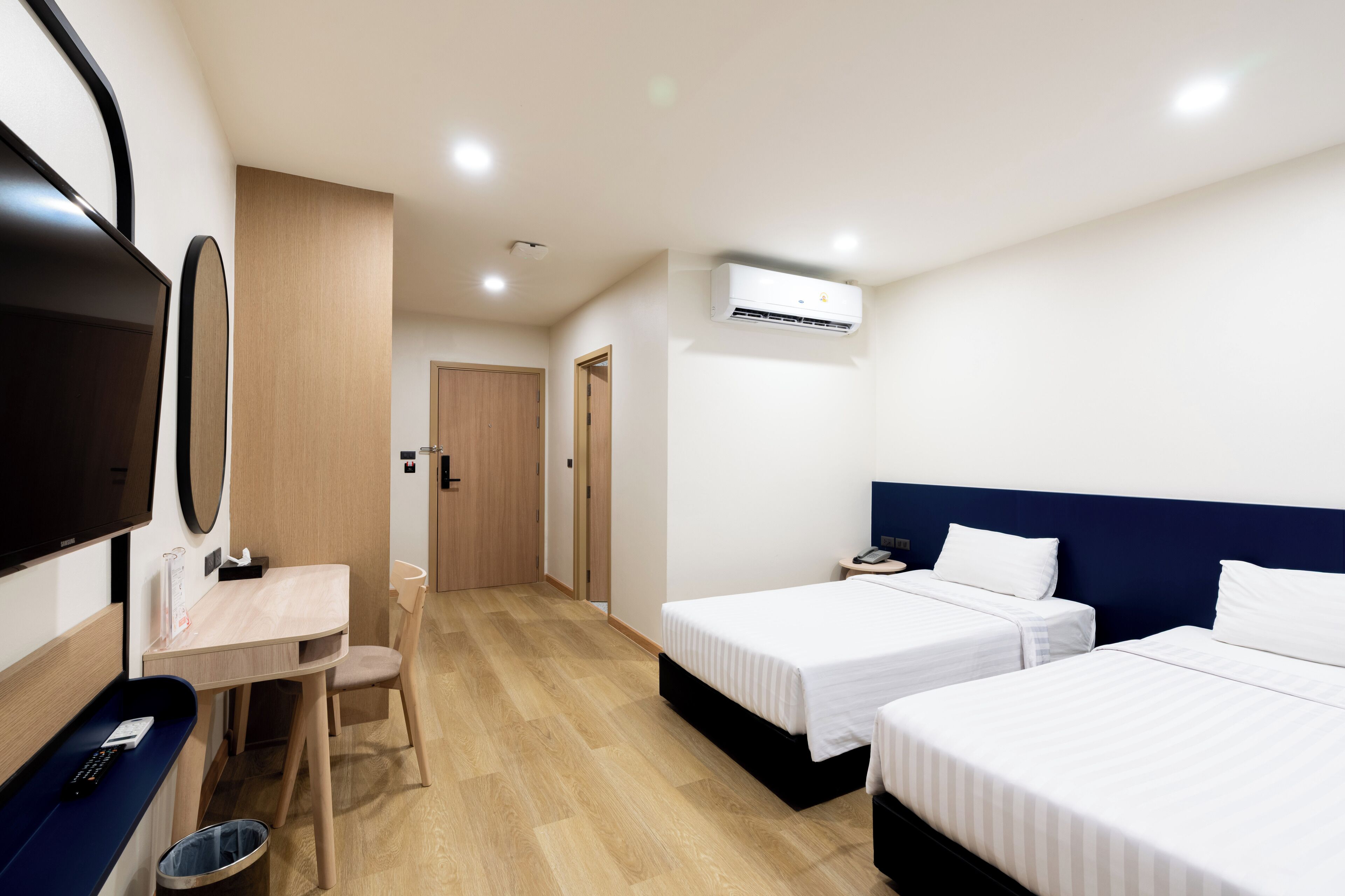 Habitación de hotel con dos camas individuales, un escritorio con silla, un televisor y un cesto de basura.