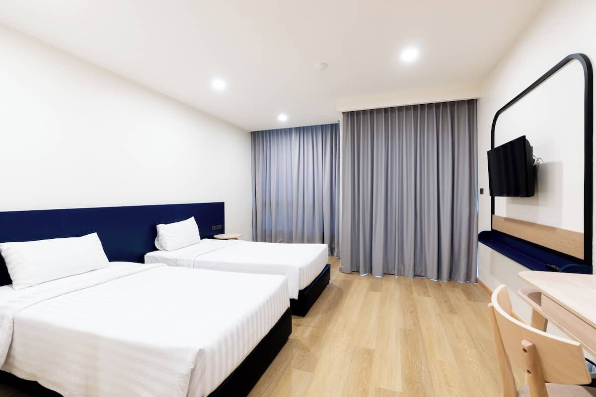 Une chambre d’hôtel avec deux lits, un bureau, une chaise, un téléviseur fixé au mur et une fenêtre avec des rideaux.