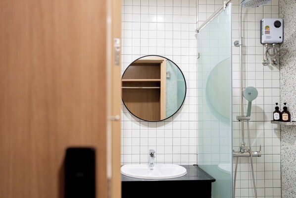 A bathroom with a round mirror, a white sink, a shower, and a toilet.
