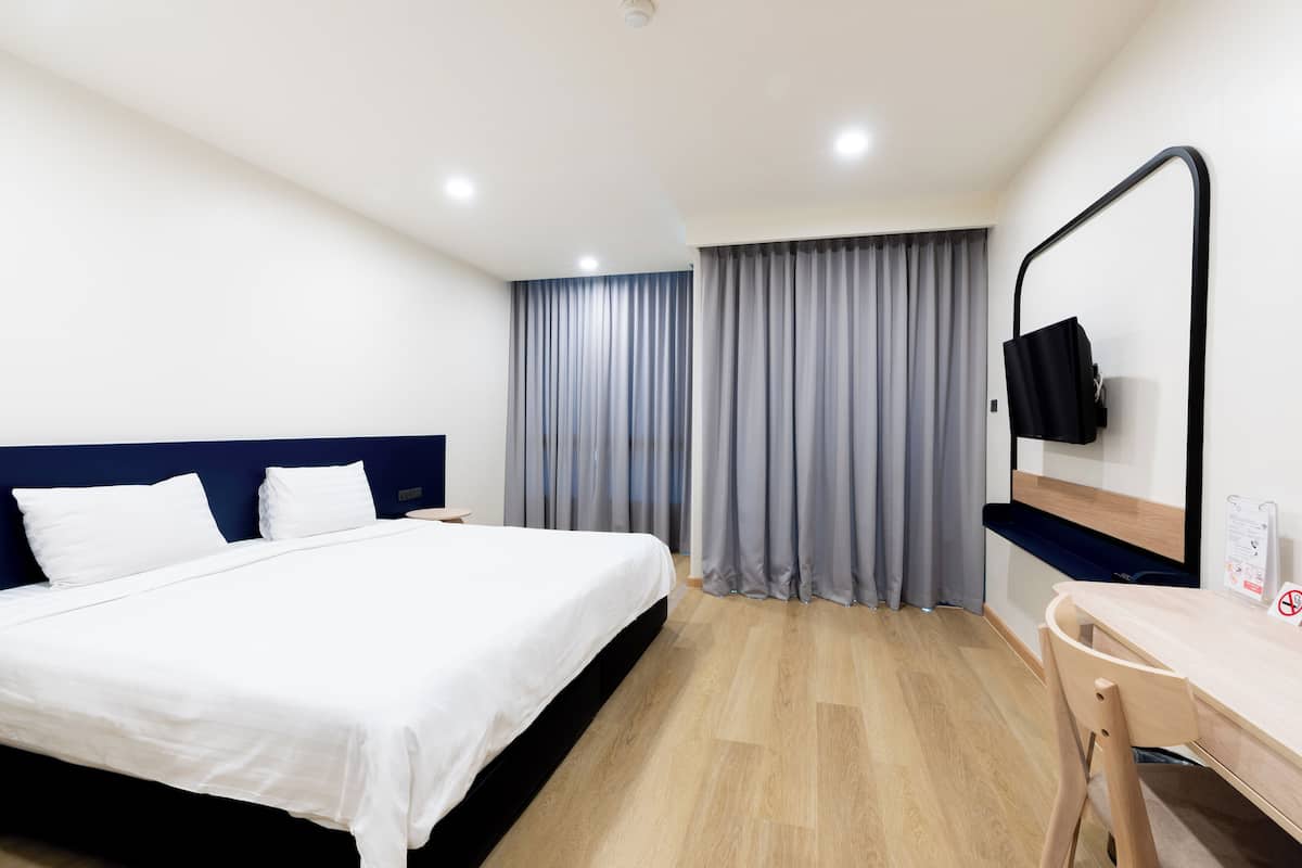 Une chambre d’hôtel comprenant un lit, un bureau, une chaise, un téléviseur fixé au mur et une fenêtre avec des rideaux.