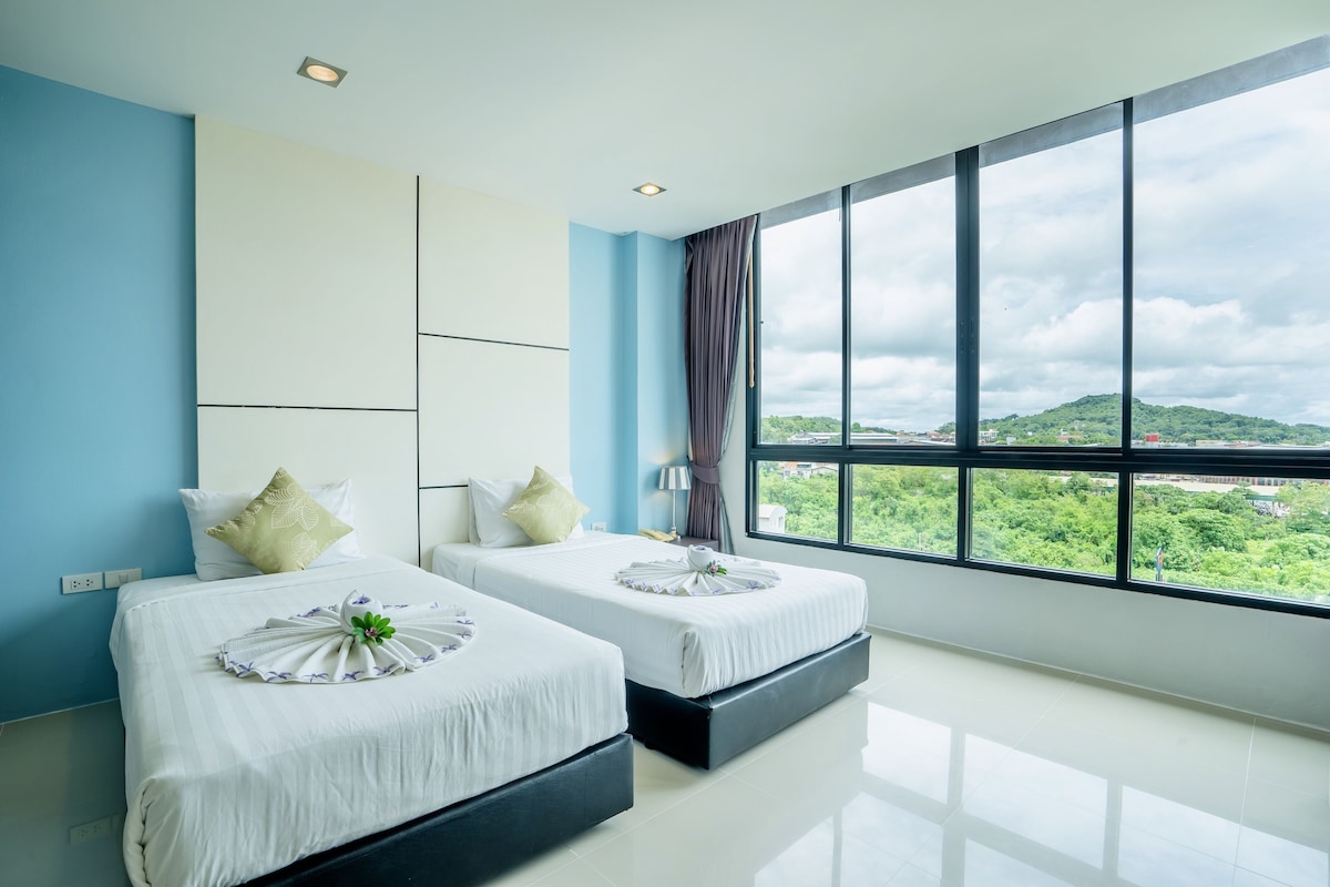A modern hotel room with two beds, a large window with a city view, and a blue accent wall.