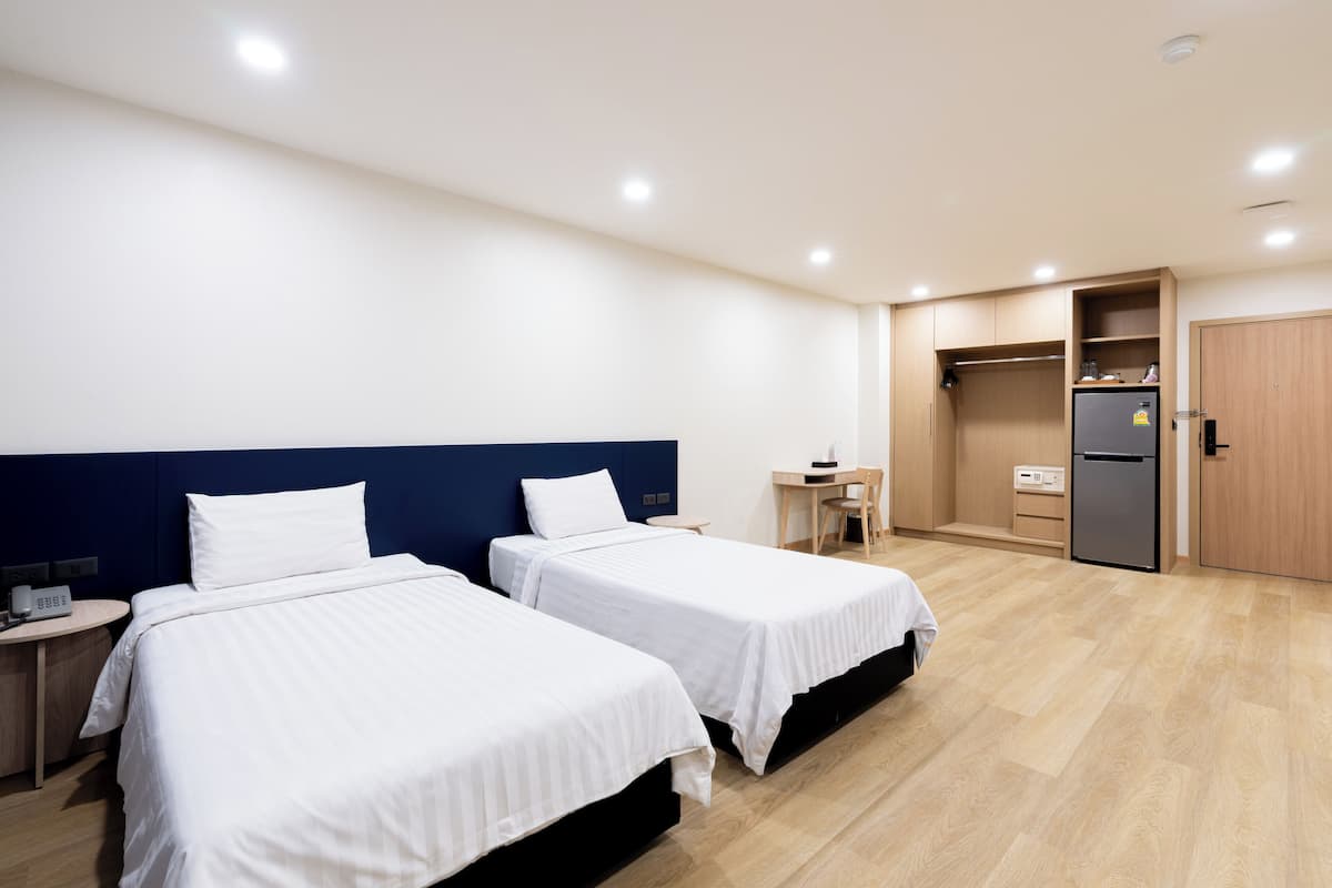 Une chambre d’hôtel avec deux lits, un bureau, une chaise, une armoire et un réfrigérateur.