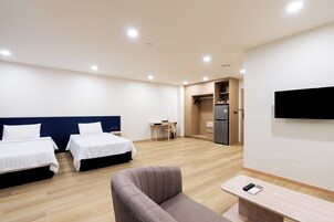 Habitación de hotel con dos camas, un sofá, un escritorio, una silla, un televisor y un refrigerador.