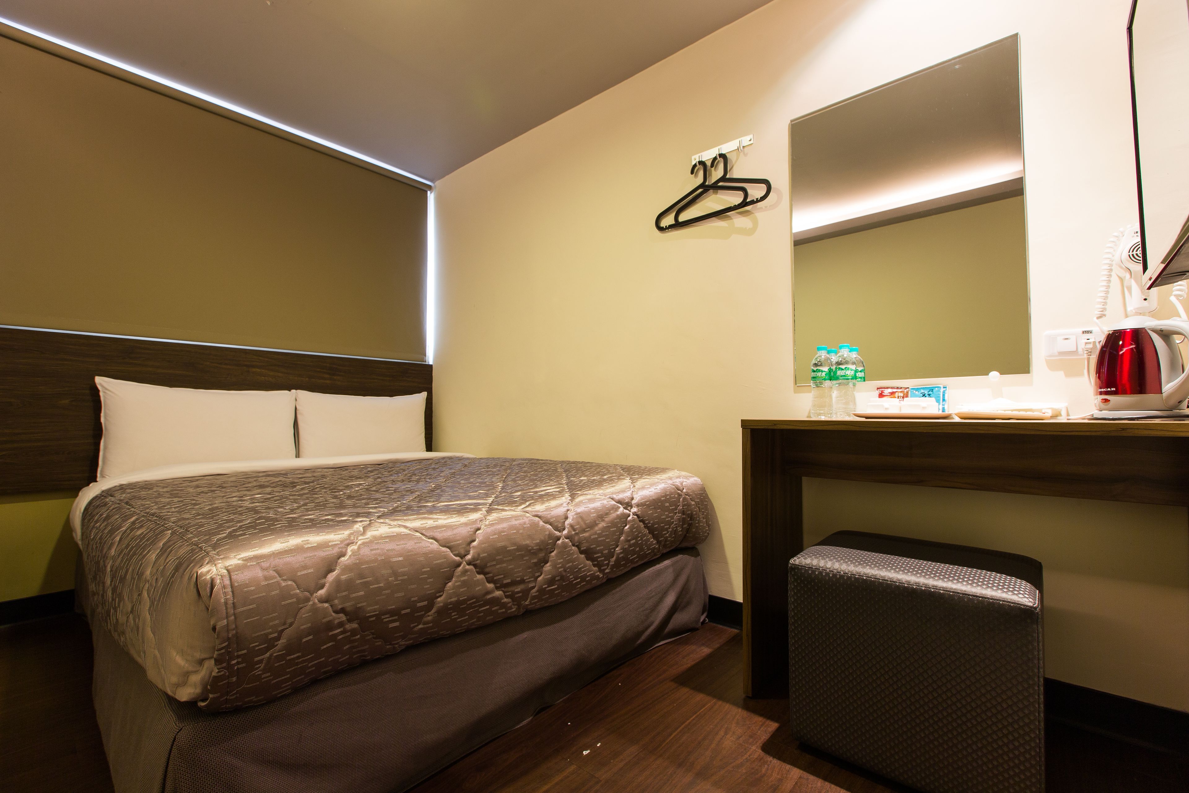 Een hotelkamer met een bed, een bureau met spiegel, een kapstok en een klein krukje.