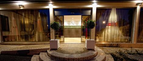 A hotel entrance with a glass facade, a central logo, and a set of steps leading up to the door.
