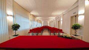 Un salón de conferencias con una larga mesa y sillas rojas, flanqueado por paredes blancas y plantas en macetas.