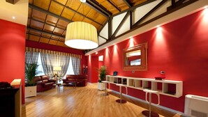 Una habitación amplia con piso de madera, paredes rojas, un ventanal con cortinas, un conjunto de sofá, una lámpara de pie y un elegante tocador blanco con repisas.
