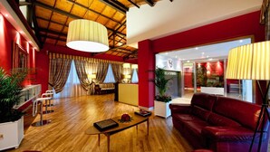 Una habitación amplia con techo de madera, paredes rojas, un sofá rojo, una mesa de centro y un área de recepción visible a través de una puerta de vidrio.