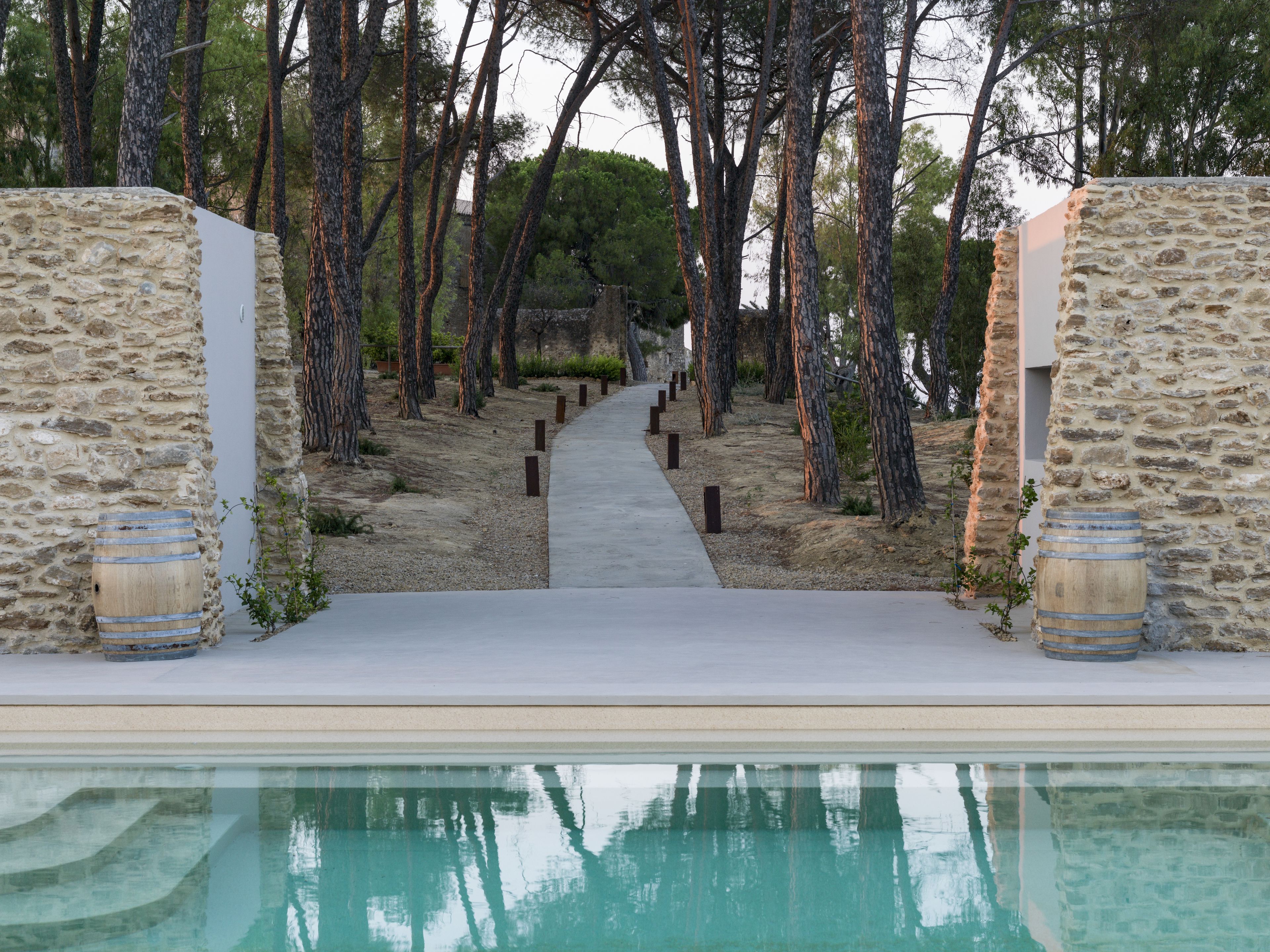 Un sendero conduce a una piscina rodeada de muros de piedra y árboles.