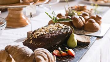 A variety of baked goods including a chocolate cake with almonds, pastries, and fresh fruits on a table.