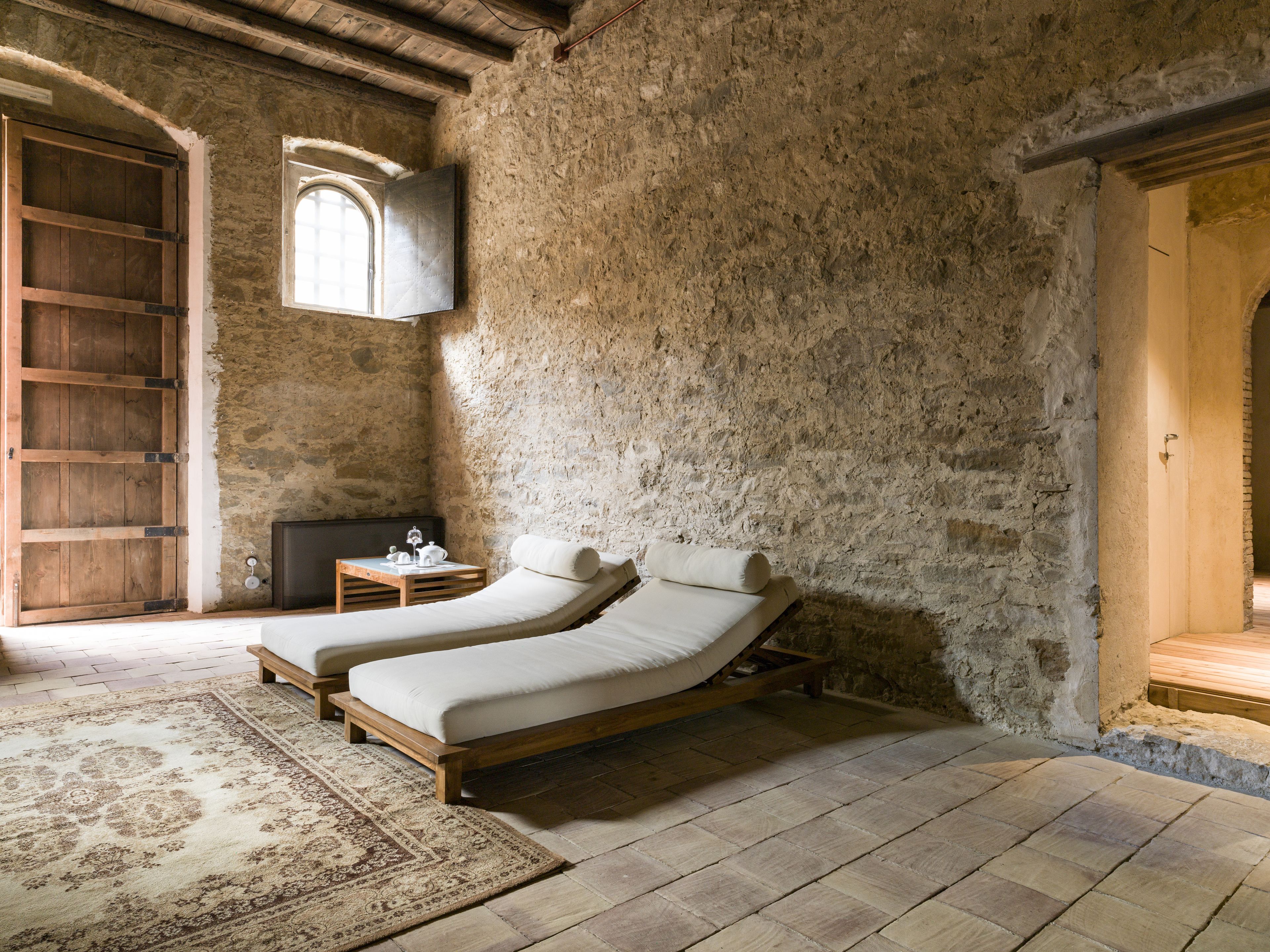 Une chambre rustique avec deux lits en bois, un mur en pierre, une porte en bois et une petite table avec une lampe.