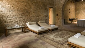 Habitació de parets de pedra amb dos llits solls, una taula de fusta i una catifes amb dibuixos.