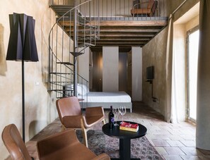 A room with a spiral staircase, a bed, a table with a book and glasses, and two chairs. - Wine Relais Feudi del Pisciotto (Niscemi)