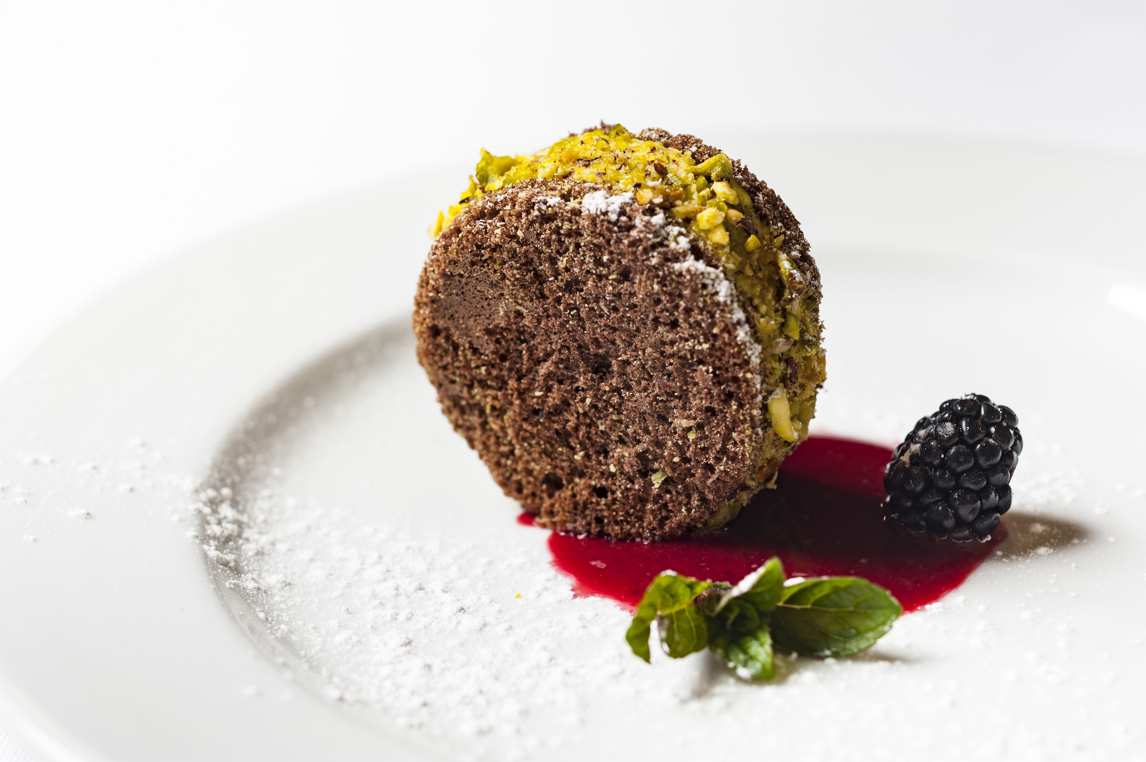 A dessert with a dark cake, a berry sauce, and a black berry on a white plate.
