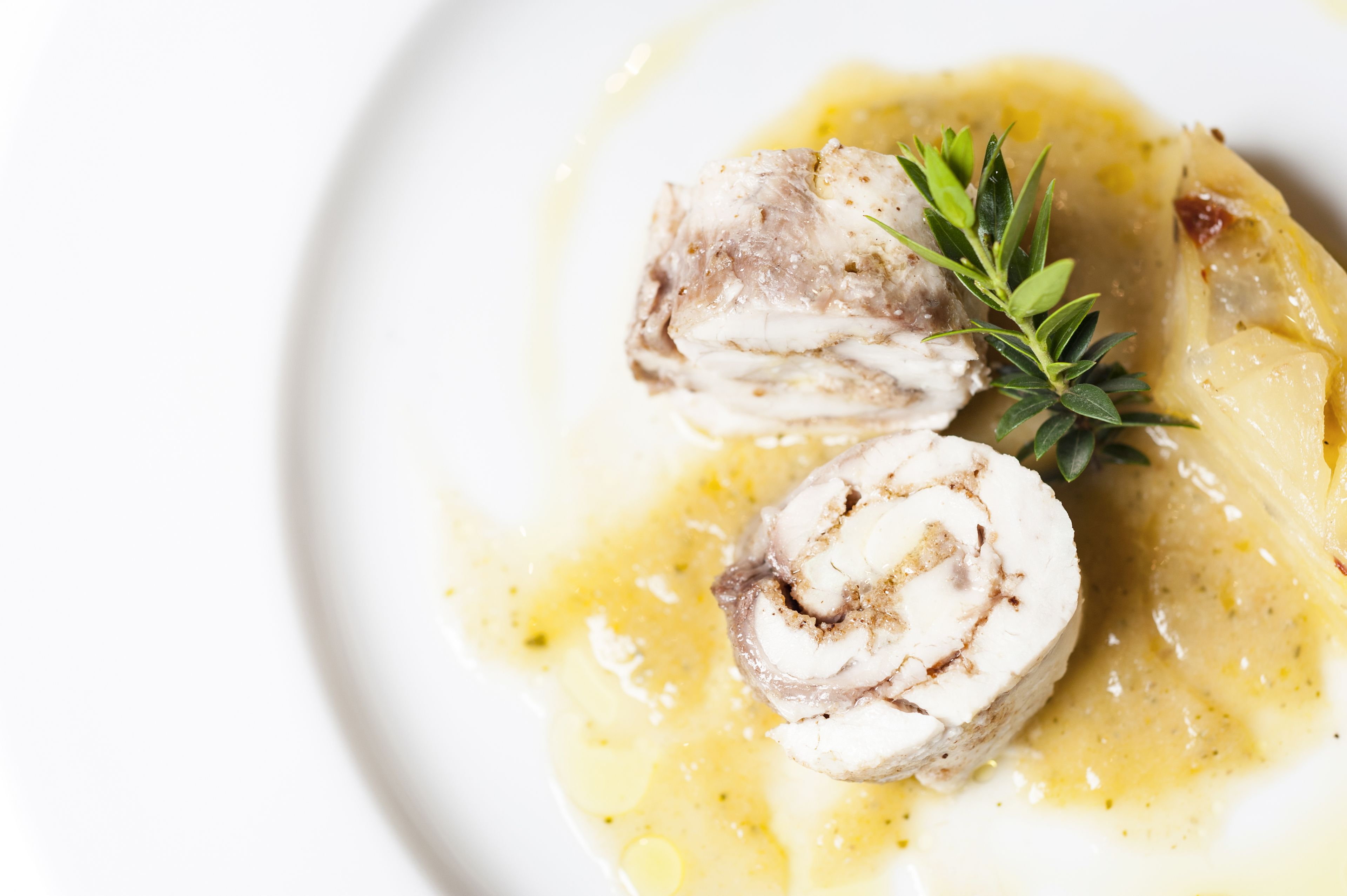 A plate with two rolled meat dishes and a sprig of rosemary.