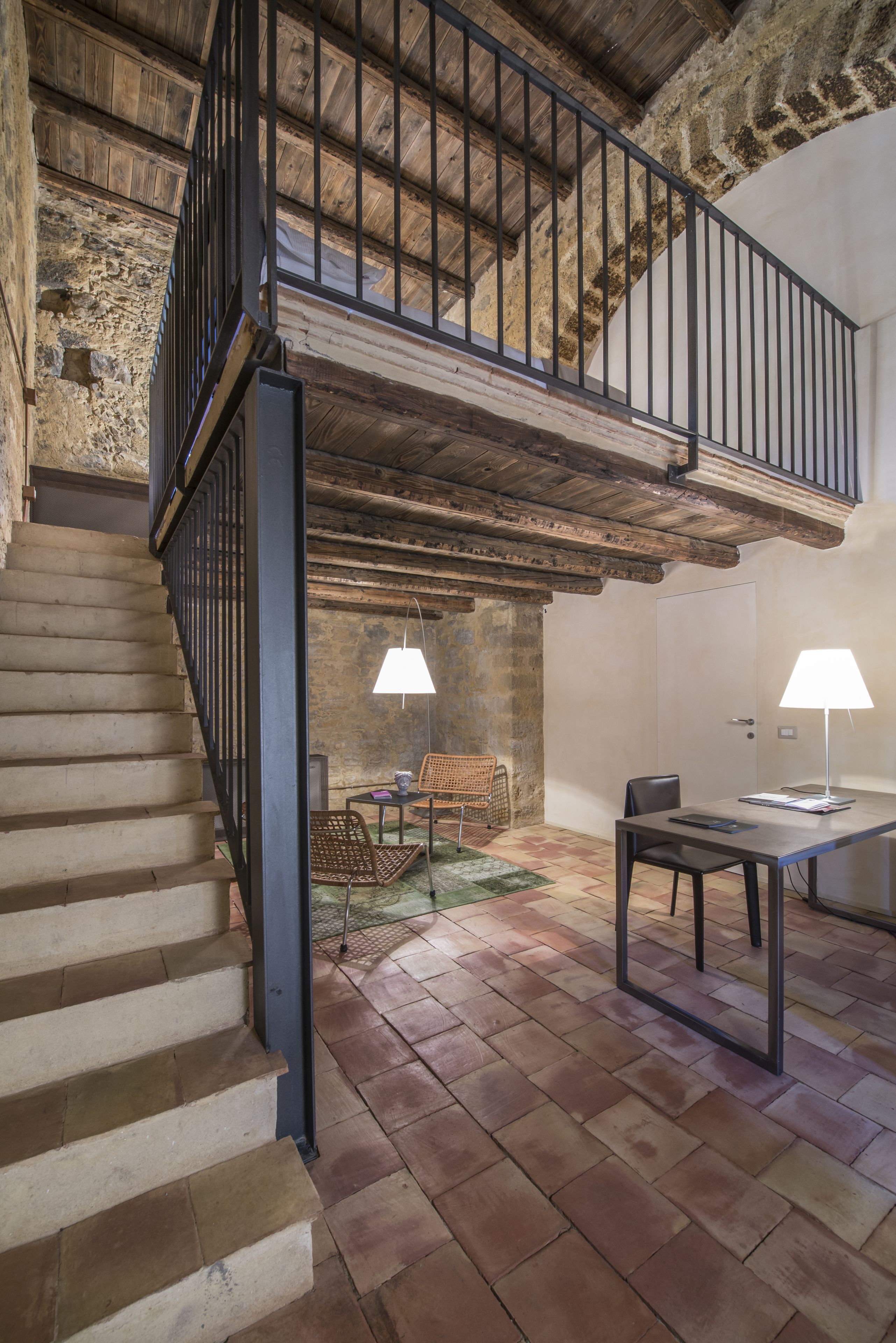 A rustic interior with a staircase, wooden beams, a dining area with a table and chairs, and two lamps.