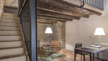 A rustic interior with a staircase, wooden beams, a dining area with a table and chairs, and two lamps.