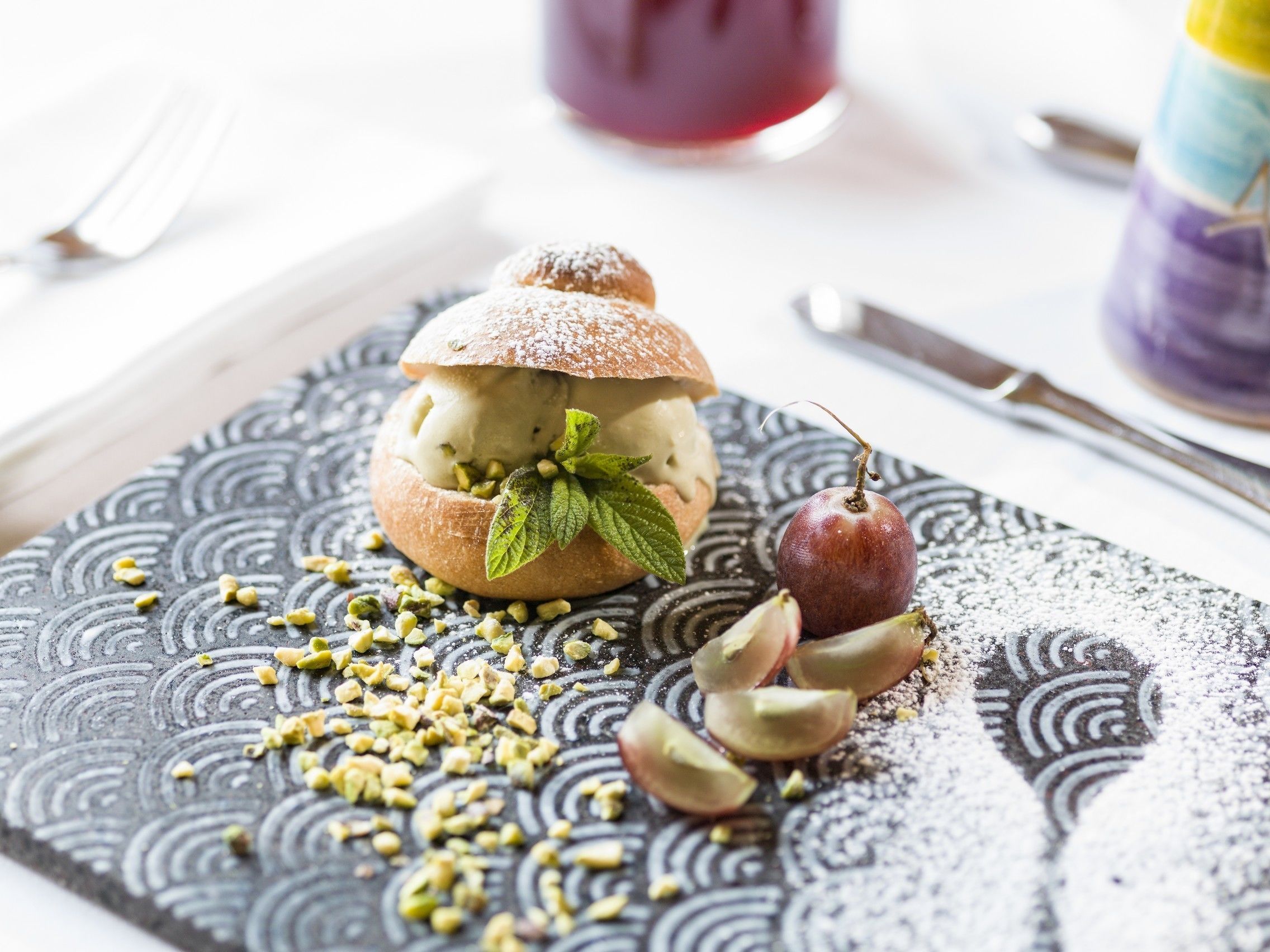 A dessert with ice cream, a cherry, and pistachios on a patterned plate.