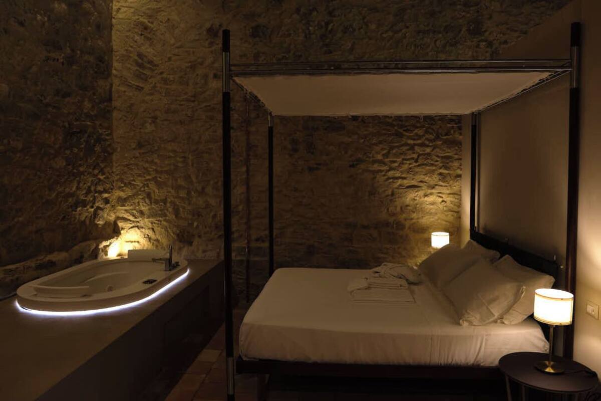 A four-poster bed with a canopy, a bathtub with illuminated edges, and a bedside table with a lamp.