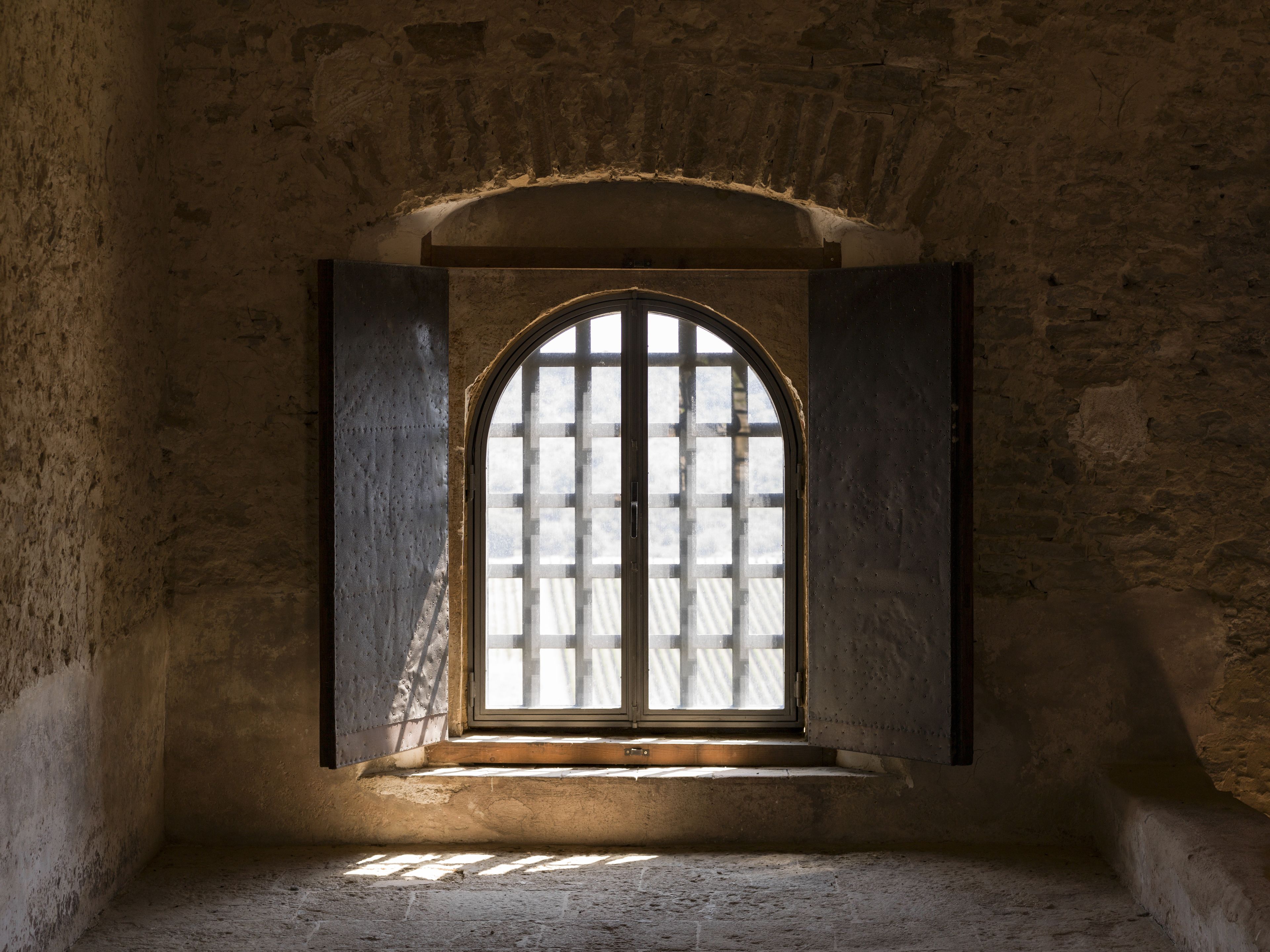A room with a single arched window, stone walls, and a wooden floor.