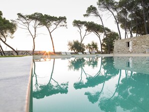 A swimming pool with clear water reflecting trees and a stone building. - Wine Relais Feudi del Pisciotto (Niscemi)