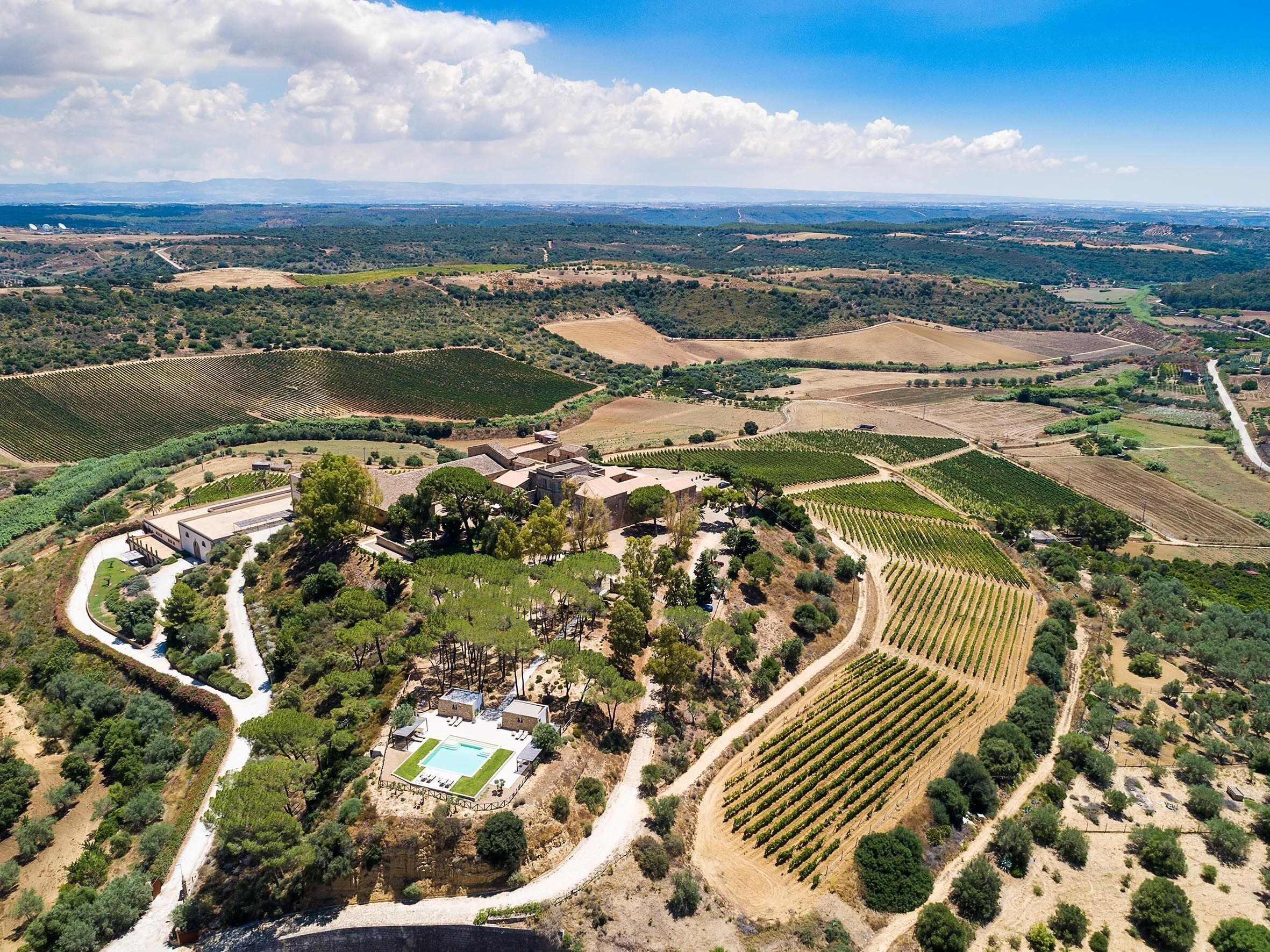 Eine Luftaufnahme eines Weingut-Anwesens mit terrassenförmigen Weinbergen, einem Schwimmbad und einem zentralen Gebäude, das von Bäumen umgeben ist.