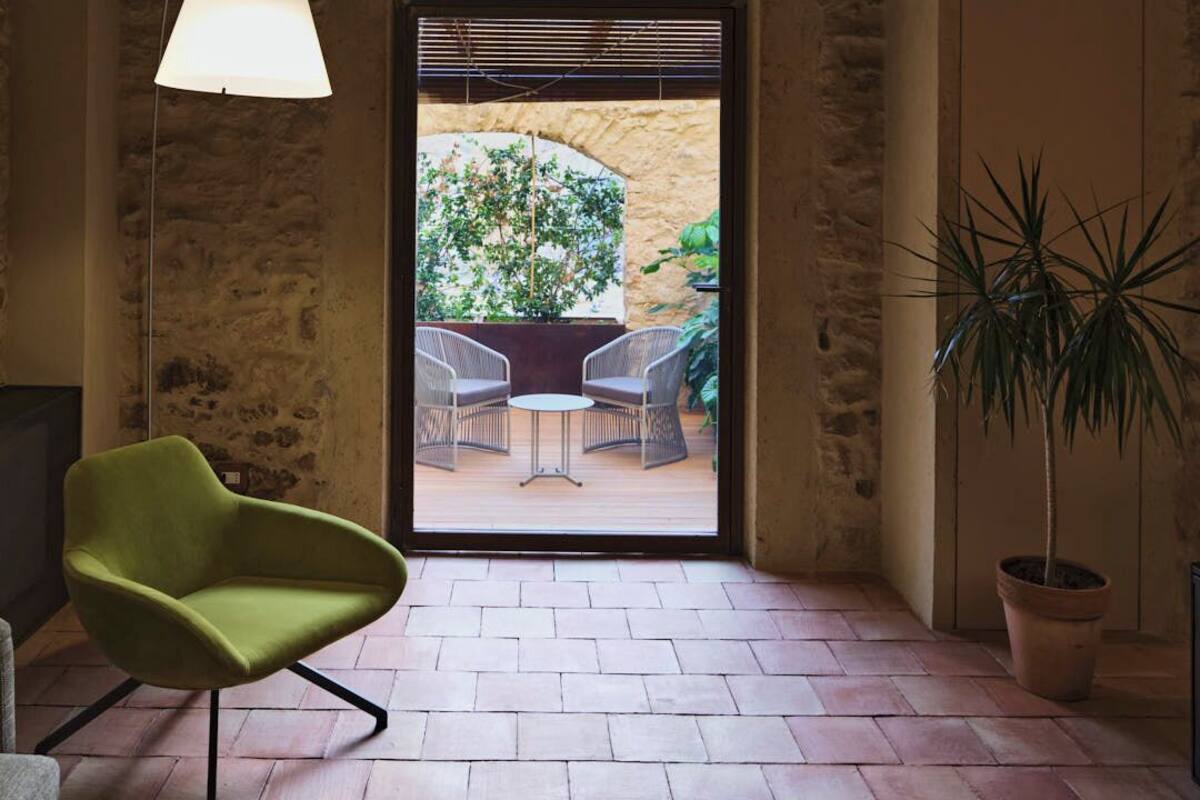A room with a green chair, a hanging lamp, and a view of an outdoor patio with chairs and a table.