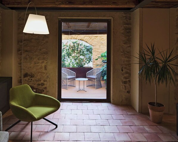 A room with a green chair, a hanging lamp, and a view of an outdoor patio with chairs and a table. - Wine Relais Feudi del Pisciotto (Niscemi)