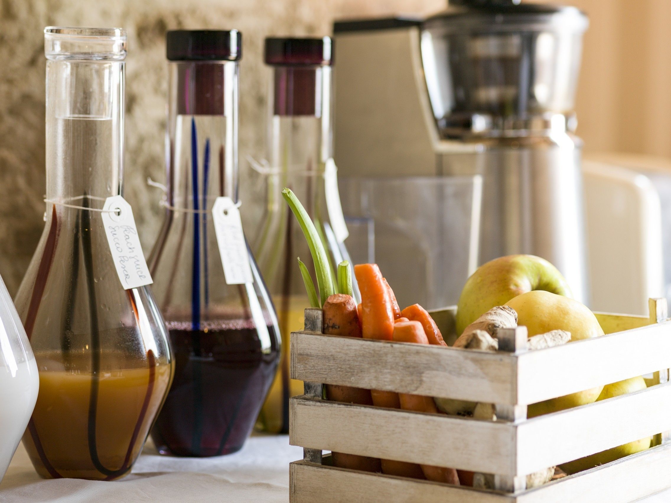 Een houten kist gevuld met fruit en groenten, en verschillende glazen flessen met etiketten.