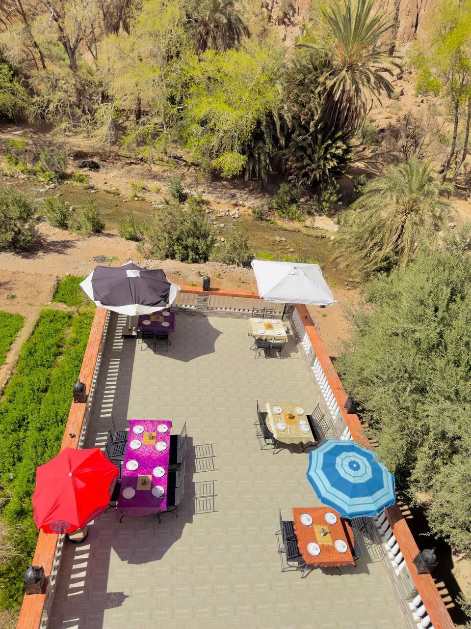 Un patio al aire libre con mesas y sillas, rodeado de vegetación y vistas a un paisaje rocoso.