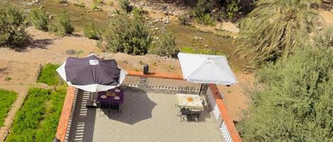 Un patio al aire libre con mesas y sombrillas, rodeado de vegetación y un paisaje rocoso.