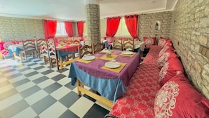 A dining area with checkered flooring, stone walls, and red curtains. Tables are set with plates and cutlery. - Auberge La Vallée (Toudgha El Oulia)