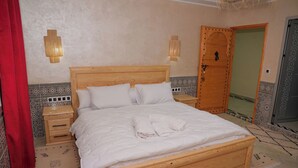 A bedroom with a wooden bed, two bedside tables, a red curtain, and patterned floor rugs. - Auberge La Vallée (Toudgha El Oulia)