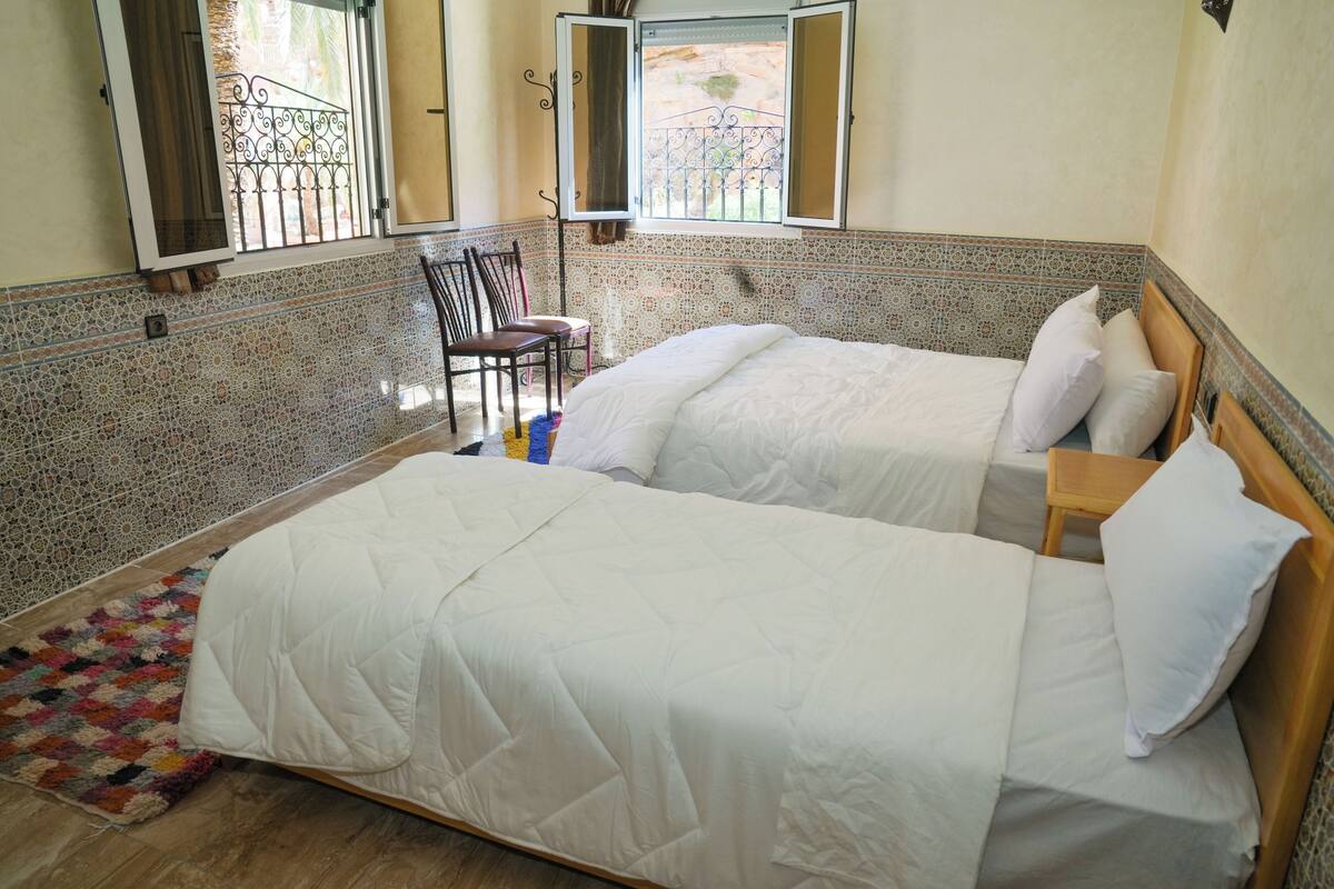 Een kamer met twee bedden, een stoel, een klein tafeltje en een raam met uitzicht.