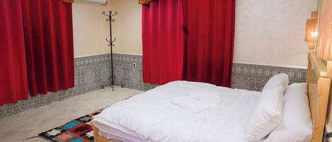 Un dormitorio con una cama, cortinas rojas, un tapete estampado y un cabecero de madera.