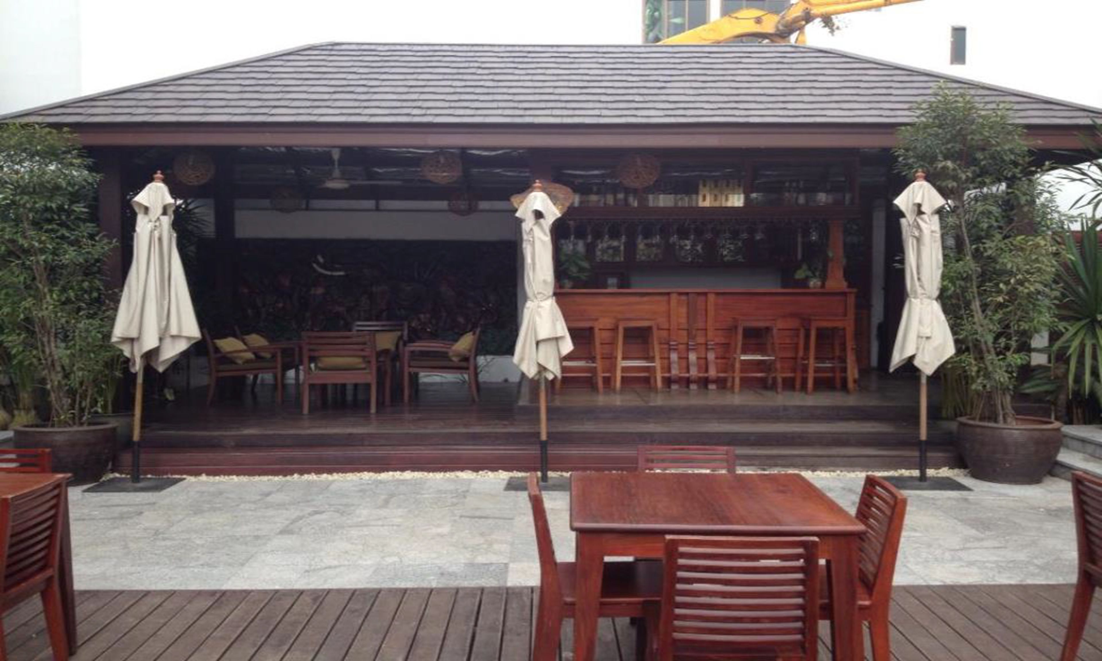 An outdoor seating area with wooden tables and chairs, umbrellas, and potted plants.